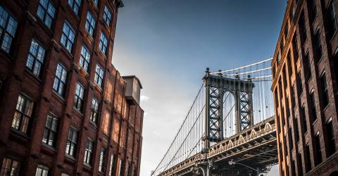 Manhattan bridge seen from a narrow alley enclosed by two brick buildings on a sunny day in summer.jpeg