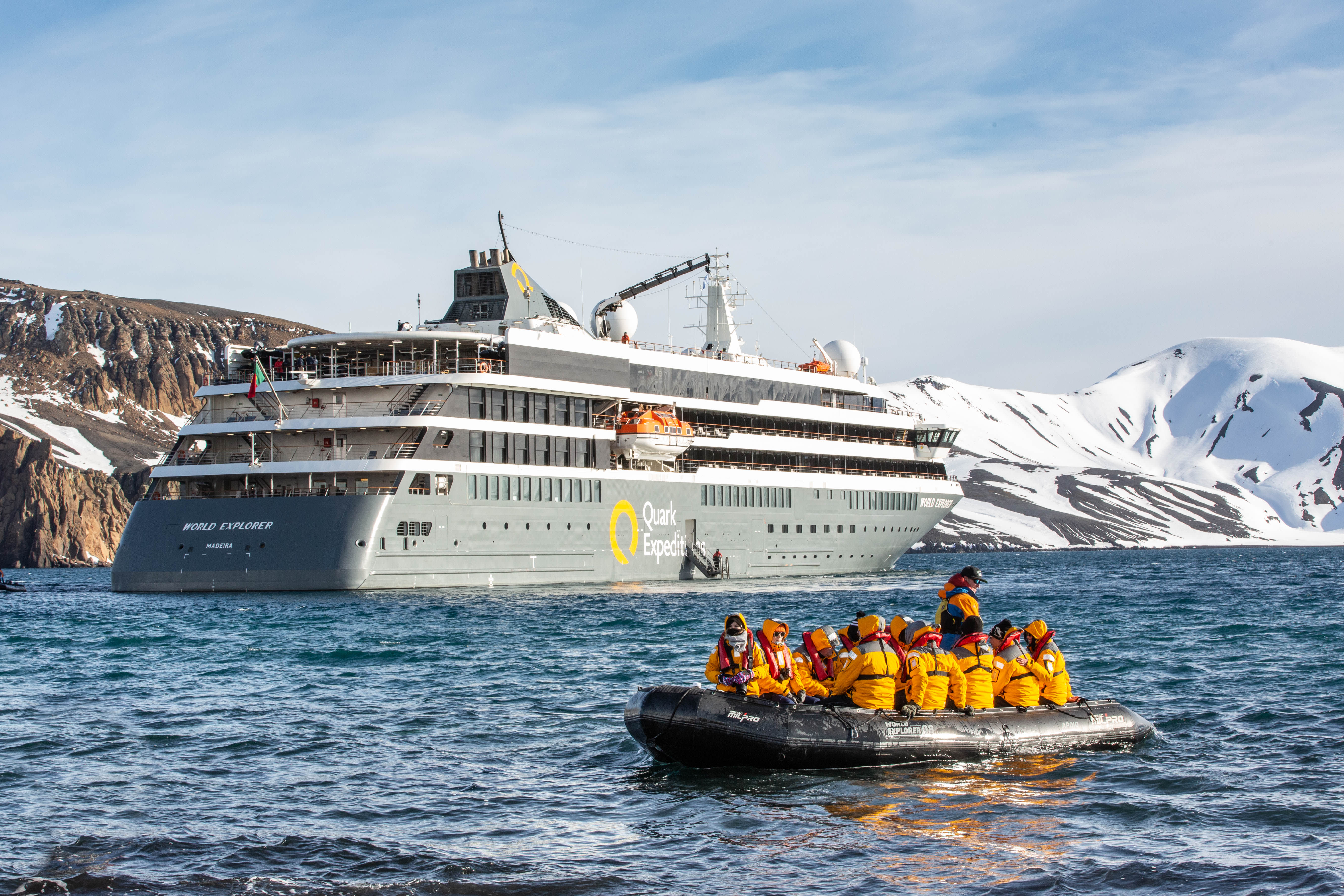 Zodiac-Boot mit Kreuzfahrttouristen im Vordergrund, im Hintergrund das Expeditionsschiff World Explorer von Quark Expeditions