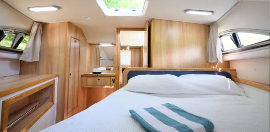Spacious double cabin aboard the Clipper with a soft white bedspread, wood-panelled furnishings, and natural light from skylights and side windows.