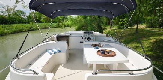 Groot bovendek van de Grand Classique met comfortabele witte stoelen, beschutte cockpit en gedekte tafel voor ontbijt, met uitzicht op het water.