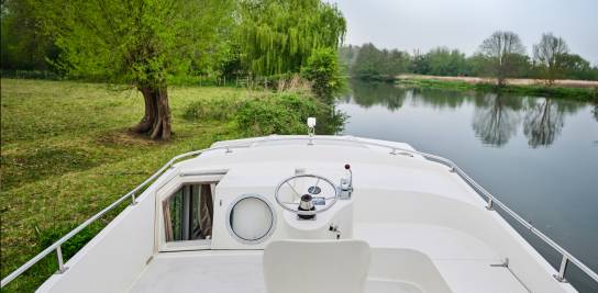 Oberdeck der Continentale mit weißem Steuerstand und Blick auf ein ruhiges Flussufer mit gespiegeltem Grün.