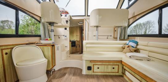 Bright and inviting saloon aboard the Caprice, with curved cream seating, wide windows, and a view through to the kitchen and helm area.