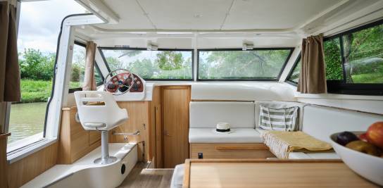 Modern Mystique boat saloon with captain's seat and panoramic windows offering a scenic river view.