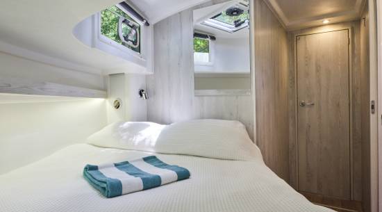 Bright double cabin aboard the Horizon 5, lit by multiple skylights and windows, with a cosy bed and wood-textured walls.