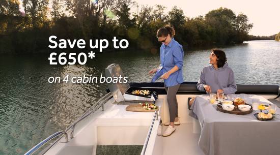 Couple enjoying a barbecue on a four-cabin boat while cruising along a peaceful river.