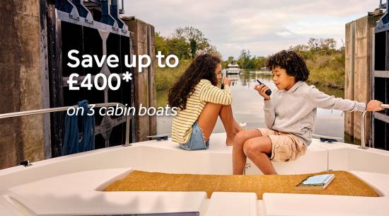 Two children relaxing at the bow of a three-cabin boat near a canal lock.
