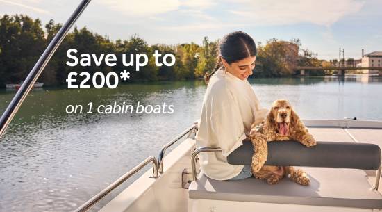 Woman sitting with her dog on a one-cabin boat, cruising past calm riverside scenery