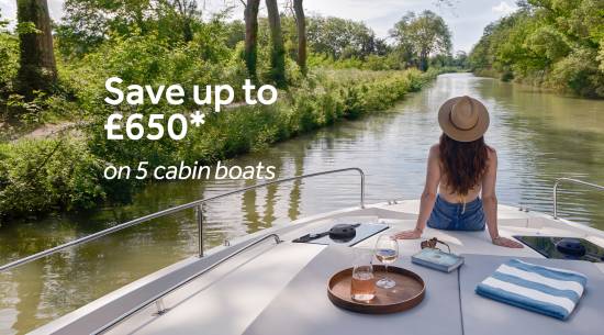 Woman relaxing at the front of a five-cabin boat, overlooking a tree-lined canal