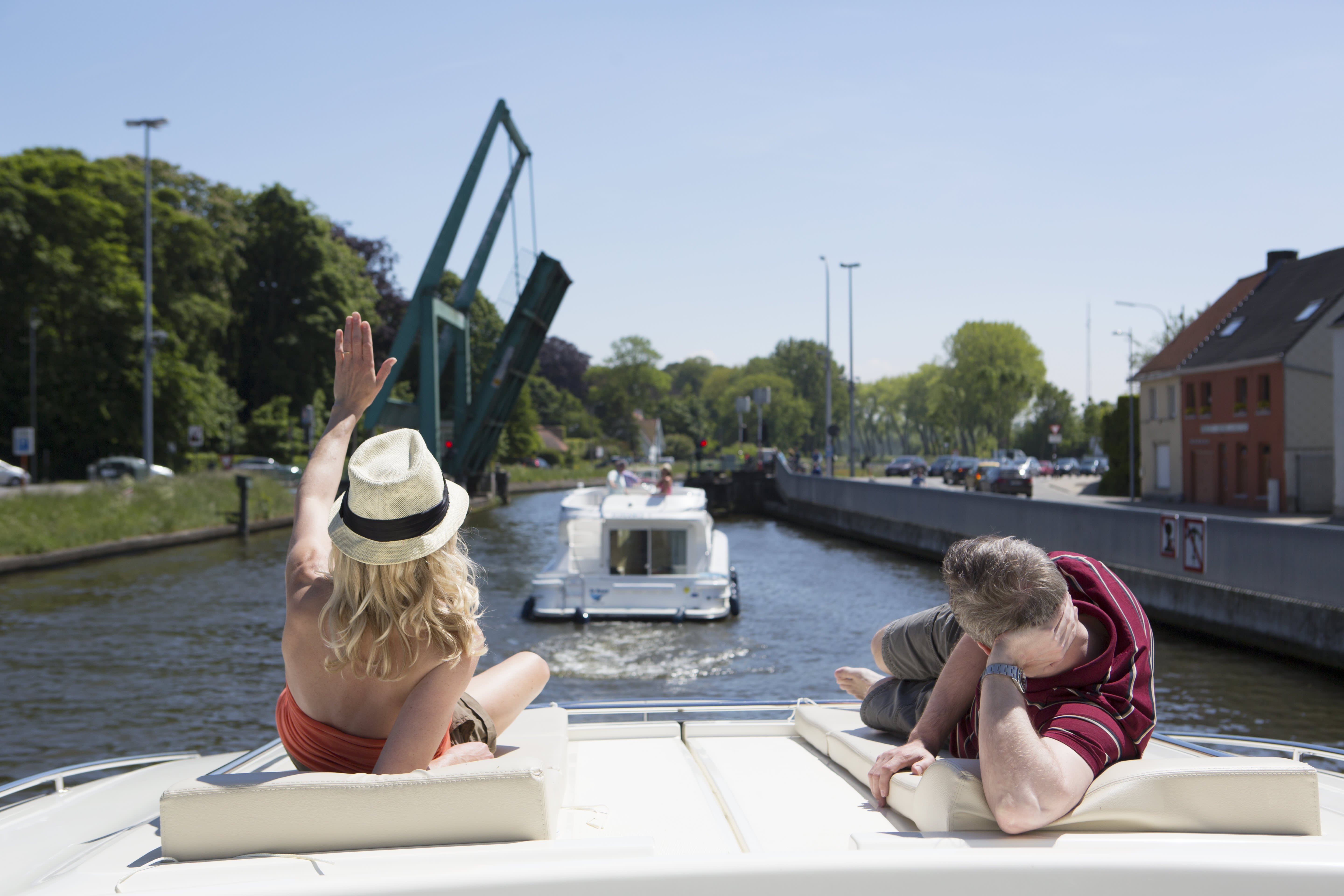 Couple relaxing on the Vision boat’s deck while cruising past a raised bridge on a sunny day.