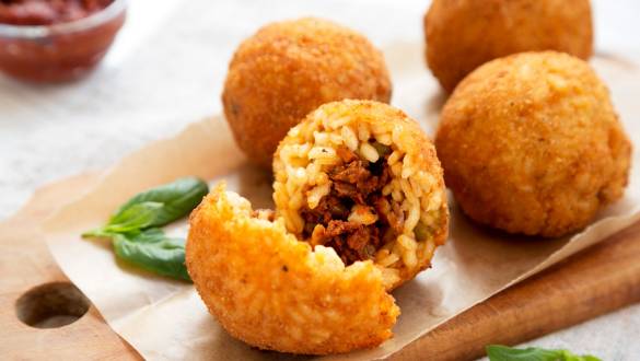 Enchanting Travels Italy Tours Homemade fried Arancini with basil and Marinara on a white wooden background, side view. Italian rice balls