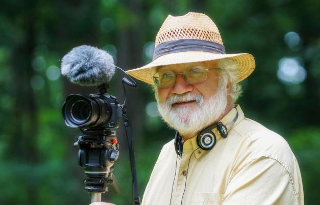 National Geographic Photographer Bob Krist standing with his camera in front of a forest