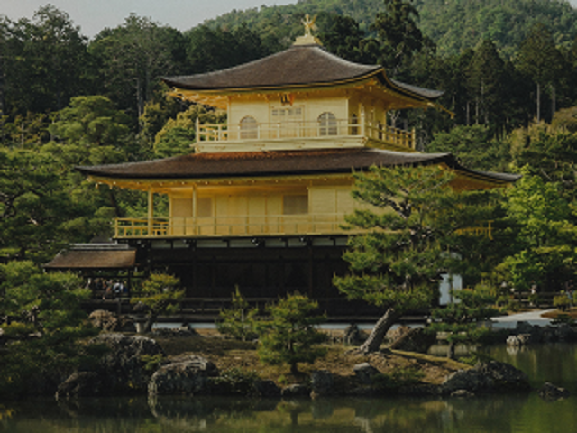 Kinkaku-ji Golden Pavilion reflecting on a calm pond, surrounded by lush green trees and forested hills in Kyoto, Japan.