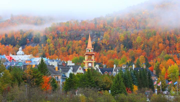 Blick auf die Kirchturmspitze des Dorfes Mont Tremblant vor der Kulisse eines nebelverhangenen Herbstwaldes