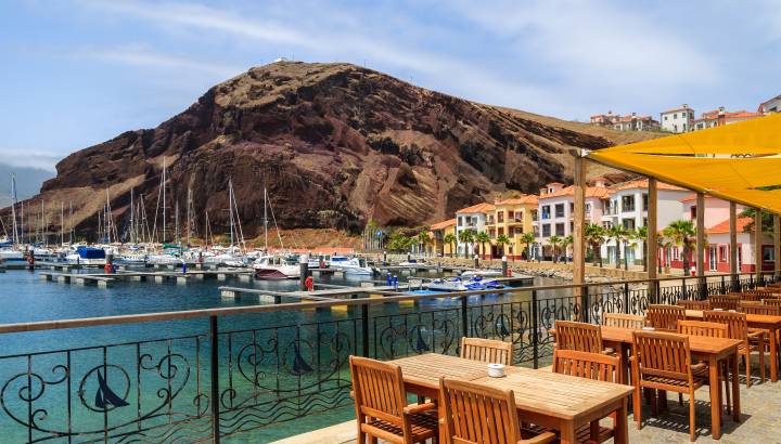 Chairs and tables of local restaurant in harbour with boats and yachts and colorful houses, Madeira island, Portugal