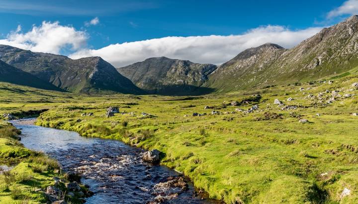Connemara landscape in Ireland - a river flows amid the meadows in front of the majestic Twelve Bens mountains