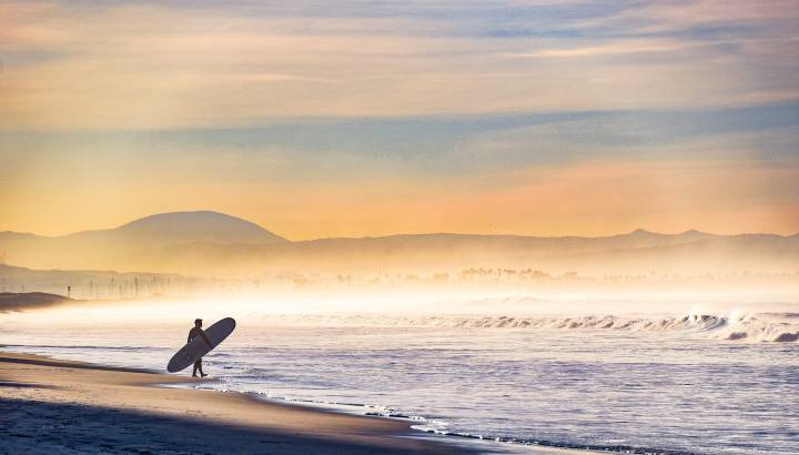 Early morning fog shrouds the coastline as this surfer enters the water in Coronado, California