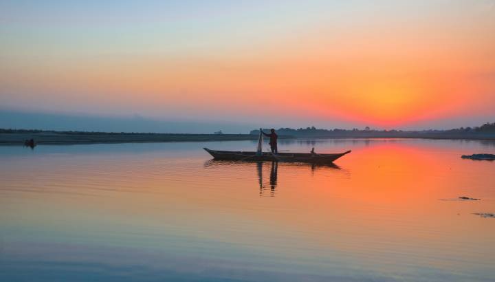 Enchanting Travels India Tours fisherman with his net and boat on the River Brahmaputra at Sunset