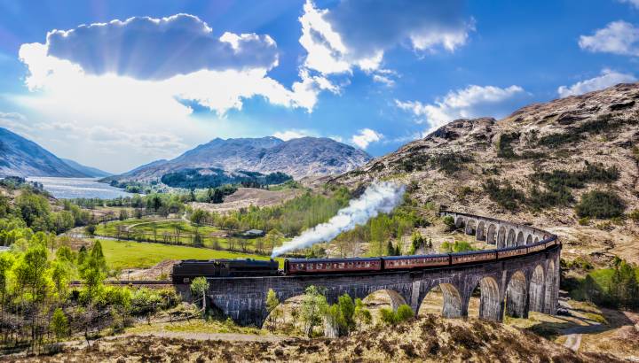Glenfinnan Railway Viaduct in Scotland with the Jacobite steam train against sunset over lake