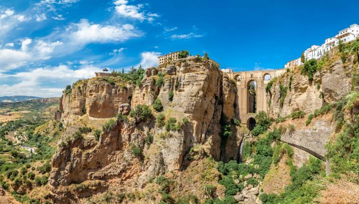 Tourists taking pictures to the Puente Nuevo bridge and the houses built on the edge of the cliff, in the ancient city of Ronda, Spain