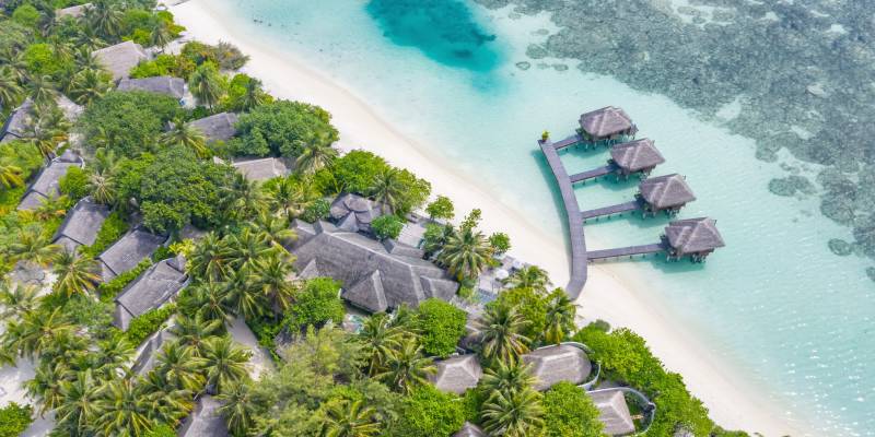 Aerial view of beautiful white sand beach, palm trees and villas, bungalows luxury beach scene of Maldives island