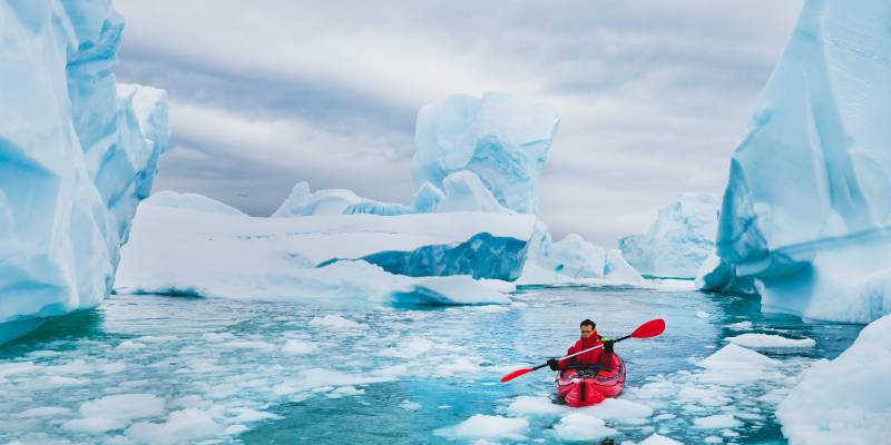 Man paddling on kayak between ice in Antractica, near Pleneau Island