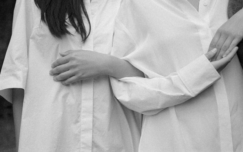Two people in white button-down shirts embracing, arms wrapped around each other, black and white close-up.