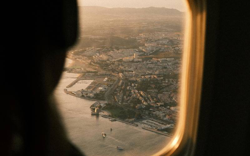 Aerial view of a coastal city with mountains through an airplane window at golden hour sunset light.