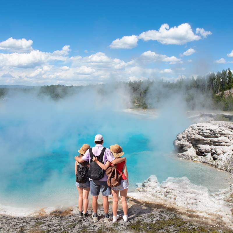 Family relaxing and enjoying beautiful view of gazer on vacation hiking trip. Father with arms around his family. Excelsior Geyser from the Midway Basin in Yellowstone National Park. Wyoming, USA