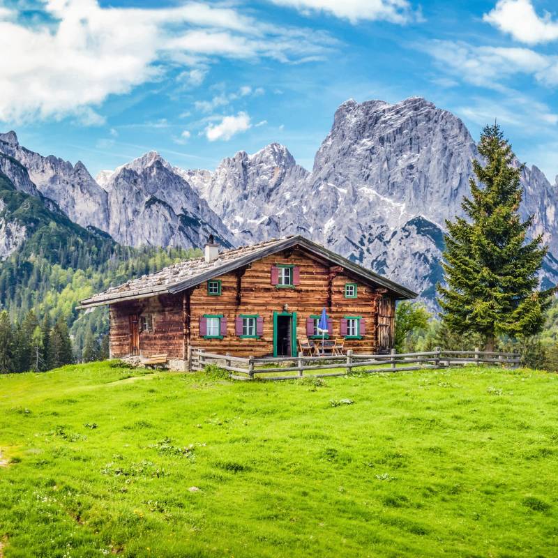 Panoramic view of beautiful mountain scenery in the Alps with traditional rural mountain chalet and fresh green meadows