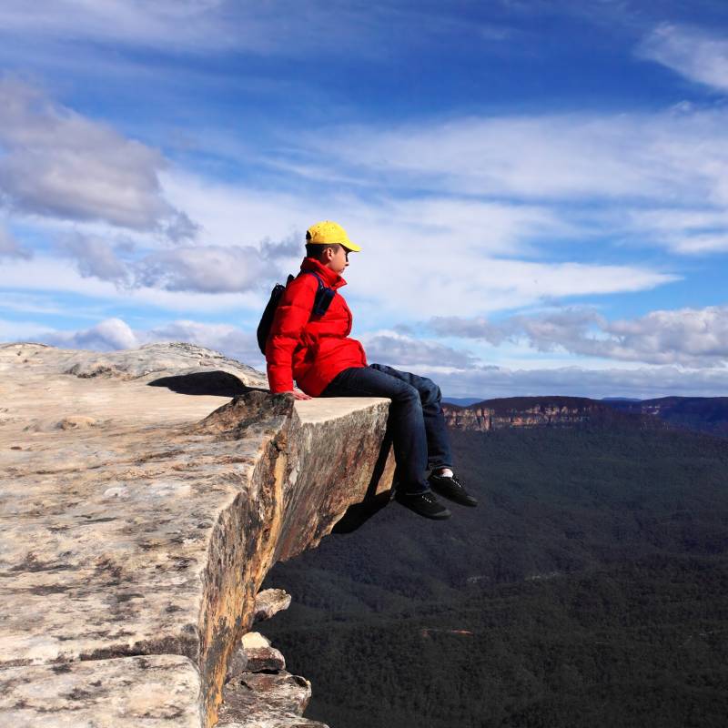 Sitting on Top of the World - hiker rests high on a cliff ledge and admires views of Blue Mountains on a beautiful sunny day.