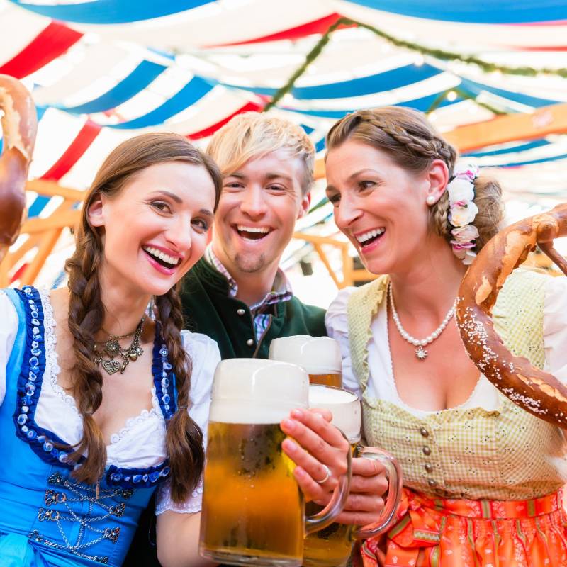Three friends in beer tent at Dult or Oktoberfest holding giant pretzels up in the air