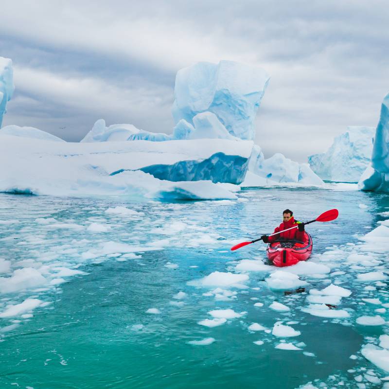 Man paddling on kayak between ice in Antractica, near Pleneau Island