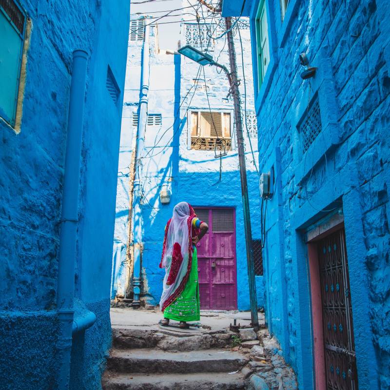 Rückansicht eine Frau in einem farbenfrohen Sari mit Kopfbedeckung in einer Gasse der blauen Stadt Jodhpur, Rajasthan Indien
