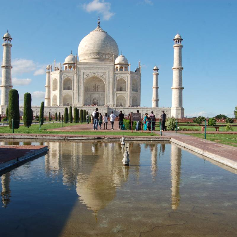 Blick über ein Wasserbecken auf das Taj Mahal an einem sonnigen Tag