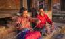 Nepali women spinning a wool in front of the house.