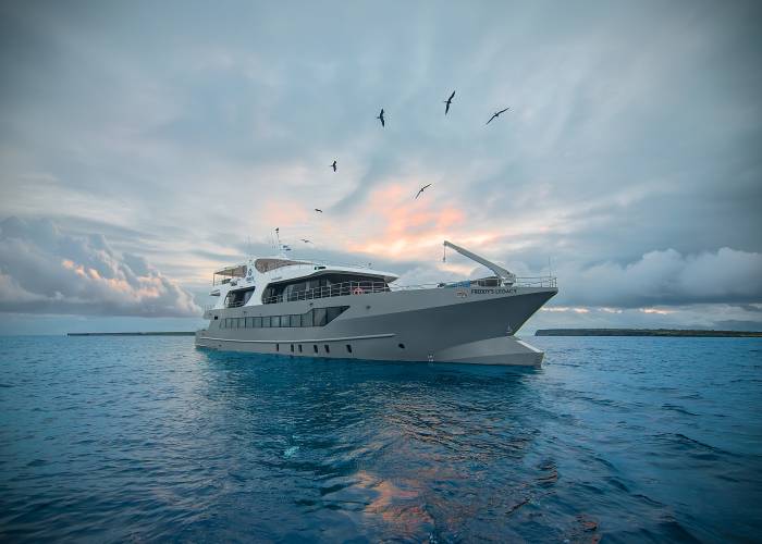 ribute liveaboard vessel stern view anchored in turquoise waters with rocky limestone islands in the background.