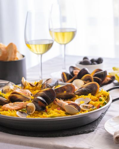 Seafood-Paella-with-prawns-clams-mussels-on-saffron-rice-and-vegetables-and-bottle-of-white-wine-on-restaurant-table