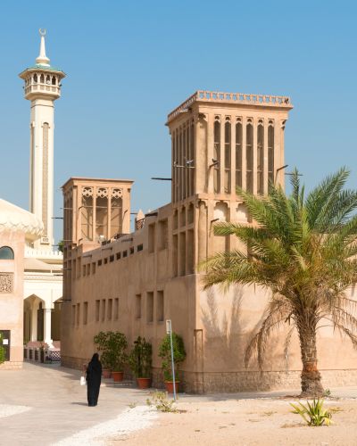 Woman-in-traditional-muslim-black-dress-in-old-arabic-city-district-with-mosque-minaret-on-background