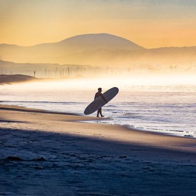 Early morning fog shrouds the coastline as this surfer enters the water in Coronado, California
