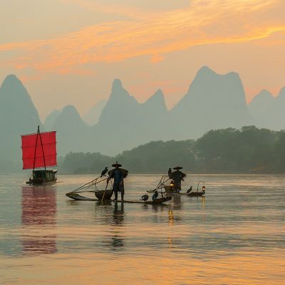 Enchanting Travels China Tours Fisherman stands on traditional bamboo boats at sunrise (boat with a red sail in the background) things to do in China