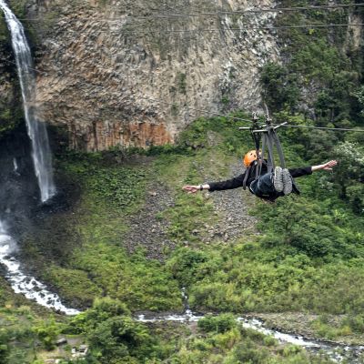 Tourist gliding on the zip line trip against Bridal veil (Manto de la novia), waterfall in Cascades route, Banos, Ecuador, South America
