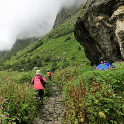 Young female climber walking down grassy rocky hill in green beautiful mountains in India
