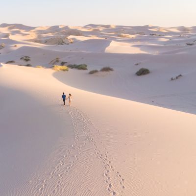 Romantic latin couple walking in the white dunes desert leaving footprints behind them. Samalayuca, Chihuahua, Mexico. Aerial shot