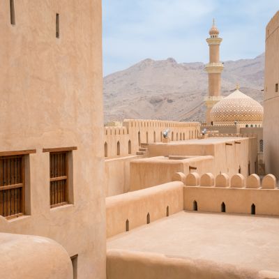 Nahaufnahme auf die sandfarbenen Fassaden der historischen Festung von Nizwa mit Minarett im Hintergrund