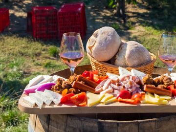 Harvesting season traditional Romanian food plate with cheese, bread, sausages, onions and red wine in glass in vineyards, on barrel