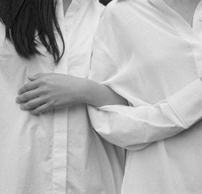 Three people in white button-down shirts embracing, arms wrapped around each other, shot in black and white.