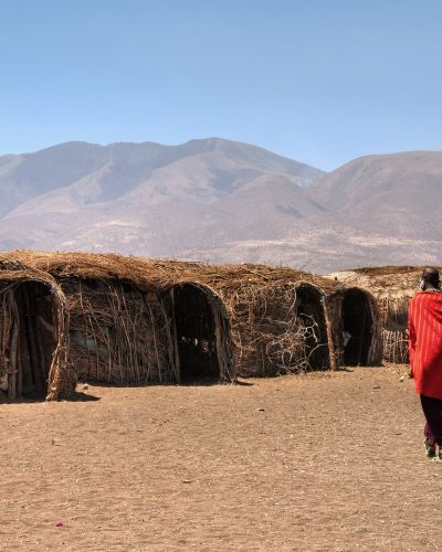 Massai huts with a woman in red in back view