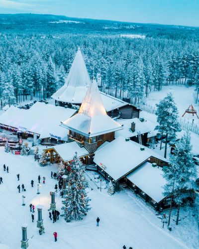 Aerial view of Santa Claus Holiday Village in Rovaniemi, Lapland, with snow-covered buildings, a lit Christmas tree, and visitors.