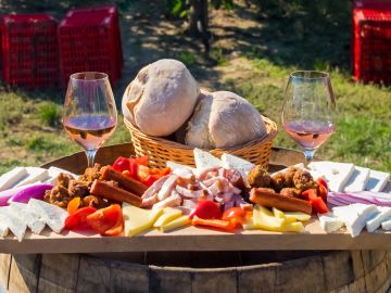 Harvesting season traditional Romanian food plate with cheese, bread, sausages, onions and red wine in glass in vineyards, on barrel