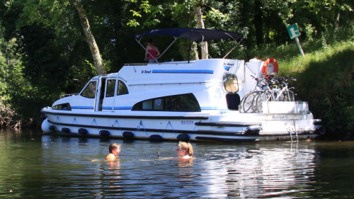 Deux personnes se baignent près d’un bateau Le Boat amarré sur les rives ombragées de la rivière Lot.
